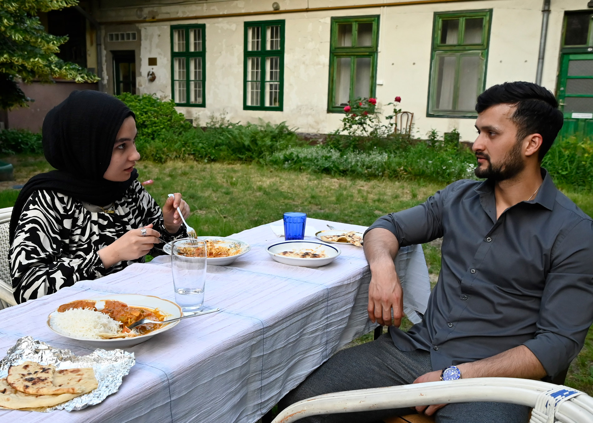 A young man and woman are having a conversation at the dinner table outside.