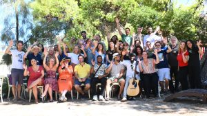 A group picture outside under pine trees. People are waving and smiling.