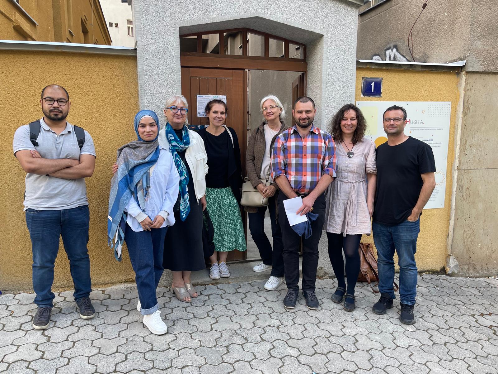 A group of people lining up outside a entrence to an old house for a picture after a poetry session.